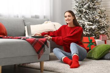 Young woman in sweater using laptop at home on Christmas eve