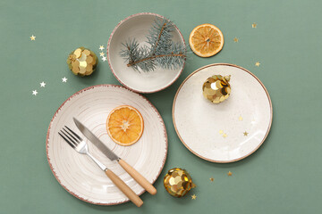 Beautiful Christmas table setting with baubles, fir branch and orange slices on green background