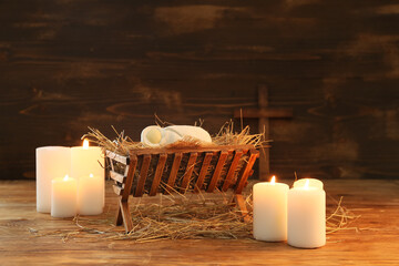 Manger with baby and burning candles on wooden background. Christmas story concept