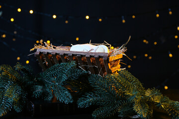 Manger with baby and fir branches on dark background. Christmas story concept