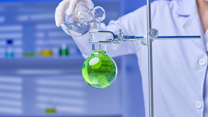 Scientist filling a flask with colored solution that is set on a stand with clear solution from the flask in their hand. high-quality photo in a contemporary lab environment.