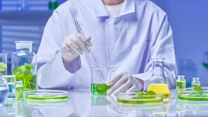 The scientist carefully stirs the green centella liquid with a glass rod in a beaker surrounded by various tools, chemicals and specimens for experiments. Sample image with modern laboratory setting.