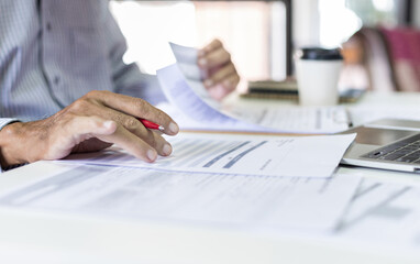 Asian businessman reviewing document report at office working with laptop, professional lawyer reading and checking financial documents or insurance contract before sign, Close-up shot