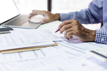 Asian businessman reviewing document report at office working with laptop, professional lawyer reading and checking financial documents or insurance contract before sign, Close-up shot