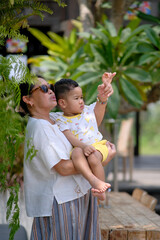 Obraz premium Side view: A middle-aged woman holding her son and pointing at something; serious, curious expression