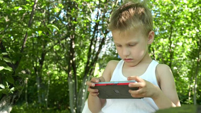 boy who is completely absorbed in playing on his cell phone misses the opportunity to interact with the environment, which can lead to harmful gadget addiction at an early age.