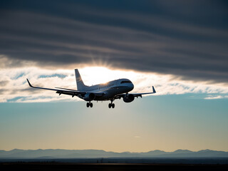 Naklejka premium a plane a plane is flying in the sky with mountains in the background.is flying in the sky with the sun behind it.