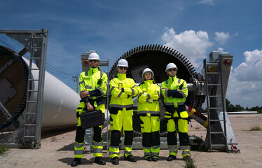 Maintenance engineer team standing prepare to work with turbines of windmills at wind turbine farm. Group of people wear safety helmet and uniform. Clean, renewable energy and sustainable technology.