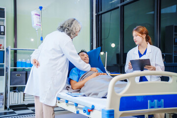 A middle-aged man lies bedridden on hospital bed, closely monitored by an old Asian woman doctor...