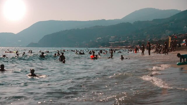 Lots of people on the beach during the summer season. The popular sandy Cleopatra Beach in Turkey. Silhouettes of people on the background of the sea, beach, and mountains.