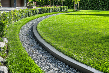 A landscaped garden featuring a curved pathway of gravel bordered by lush green grass and neatly trimmed hedges.