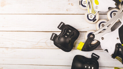 Set of roller skates and protective gear set - knee, elbow and wrist pads and helmet in yellow colors on wooden background flat lay. copy space