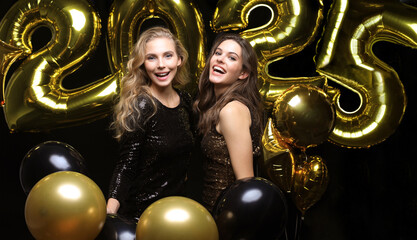 Happy gorgeous girls in stylish sexy party dresses holding gold 2025 balloons, having fun at New...