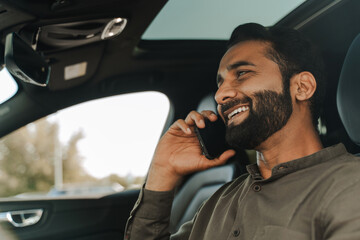 Smiling, handsome Indian businessman talking on the phone while driving car