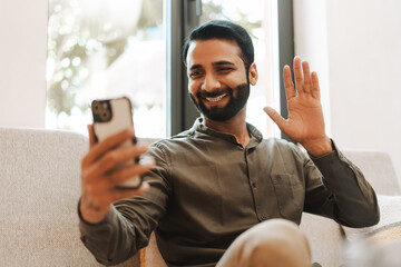 Happy businessman, smiling Indian man making video call holding mobile phone, waving hand