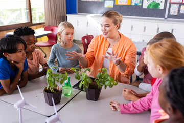 In school, female teacher explaining plant growth to diverse group of diverse students in classroom