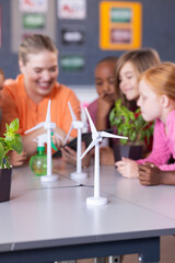 In school, female teacher and diverse students examining wind turbine models and plants together