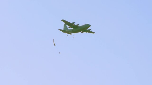 Military C-130 Hercules is shown releasing paratroopers and cargo during an airborne mission. This tactical operation showcases capabilities of the aircraft for troop deployment and logistics support