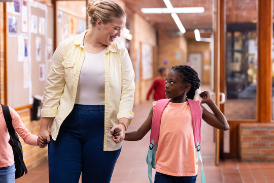Walking in school hallway, female teacher holding hands with smiling diverse students