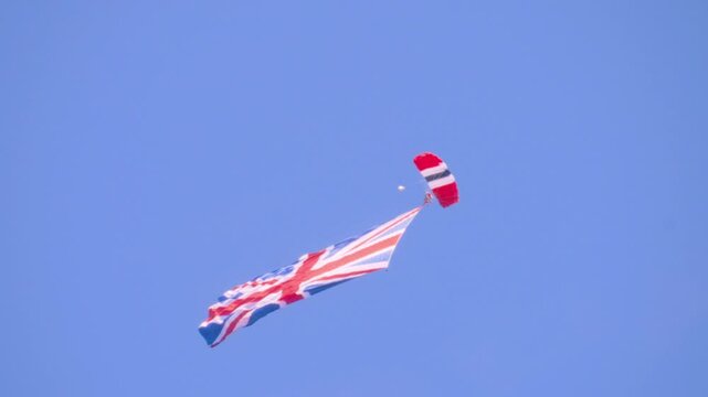 British Red Devils parachutist gracefully descends through sky, proudly displaying Union Jack flag. Red, white, and blue colors of parachute complement iconic flag in this military demonstration