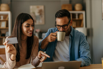 The couple enjoys shopping online or booking vacation tickets together, sitting in their cozy home