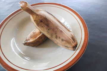 brown boiled bananas on a light brown plate with a dark background