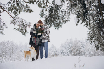 Happy young couple with akita dog in forest on winter day