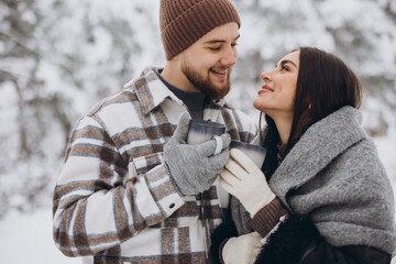 Happy beautiful couple resting and drinking hot tea in the forest in winter in the mountains