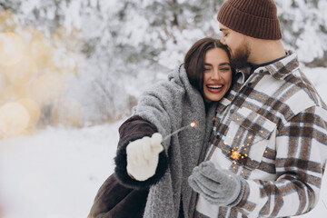 Happy romantic couple in love holding sparklers in snowy winter forest