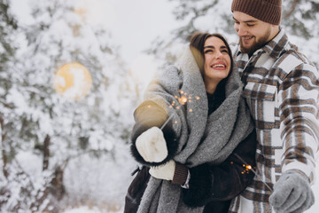 Obraz premium Happy romantic couple in love holding sparklers in snowy winter forest