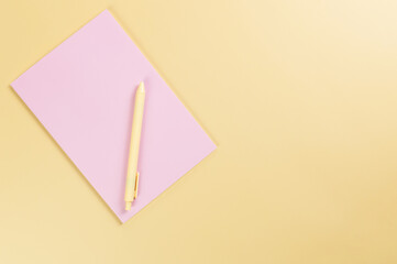 Top view of pink notebook, yellow pen on yellow background. School, office wallpaper. Flat lay, copy space.