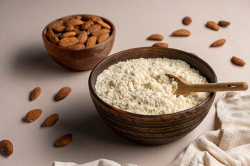 Almond milk in glass, flour in wooden brown spoon and nut kernels. Vegan or keto diet concept.