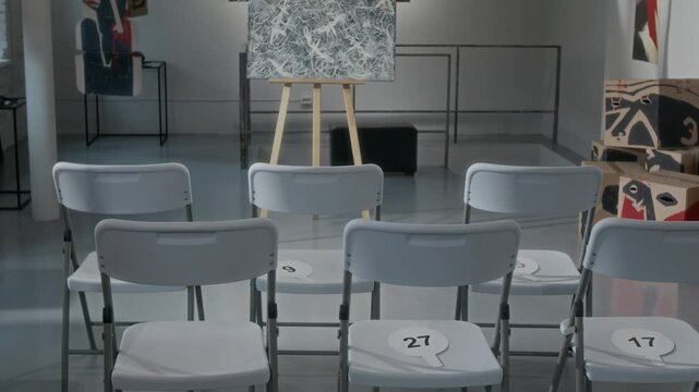 Full no people shot of monochrome abstract painting displayed on easel at contemporary art gallery or museum, rows of chairs with number cards, prepared for auction