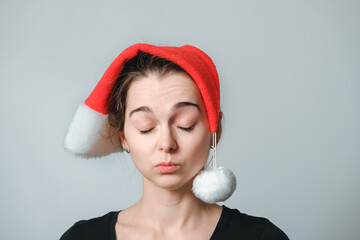 Portrait of young woman in Santa Claus hat on gray background. The concept of stress and fatigue,...
