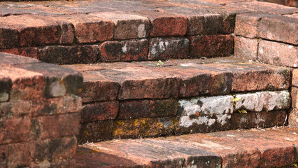 Old brick stairs showing signs of age and wear, with moss and lichen growing between the cracks. The earthy tones and weathered texture evoke a sense of history and decay