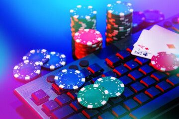 A vibrant arrangement of poker chips and playing cards on a gaming keyboard with a mouse at an online casino setup during the evening