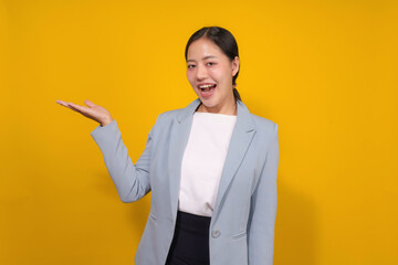 Asian businesswoman wearing a blue blazer is gesturing with her hand and smiling on a yellow background