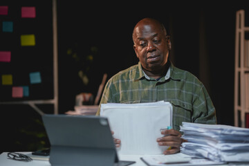 Senior black employee is working late in the office reviewing documents at his desk
