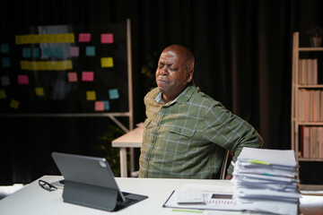 Senior manager is working late in the office and having back pain from sitting too long in his chair