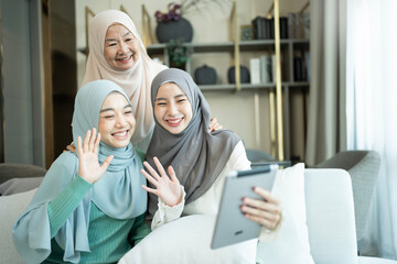 Muslim mother and two daughter using tablet making video call in a living room 