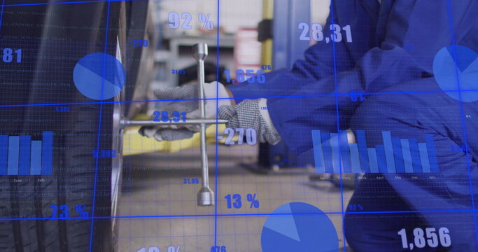 Image of financial data processing over male african american car mechanic fixing tyre - Powered by Adobe