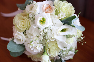 A beautiful wedding bouquet of roses and gold wedding rings on it.