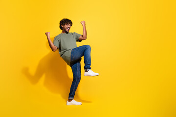 Full size photo of ecstatic guy dressed khaki t-shirt jeans scream yeah raising fists up win bet isolated on yellow color background
