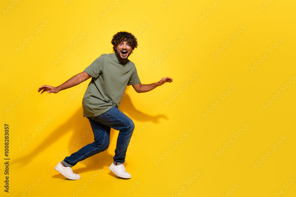 Wall mural Full size photo of funky guy dressed khaki t-shirt jeans steal on tiptoes near promo empty space isolated on yellow color background