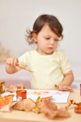 happy little child girl painting autumn leaves. baby girl drawing leaves in yellow and orange paint