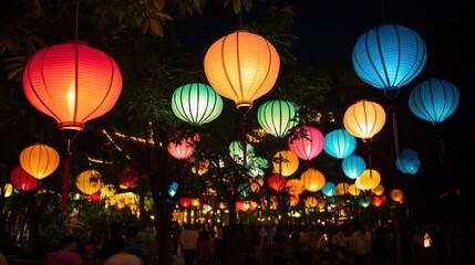 Colorful lanterns hanging from trees illuminate a gathering of people at night.