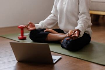 A curly African American woman in activewear practices yoga in a serene living room Meditating at Home with Headphones setting.
