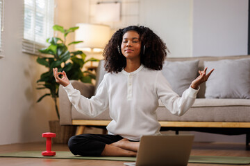 A curly African American woman in activewear practices yoga in a serene living room Meditating at Home with Headphones setting.
