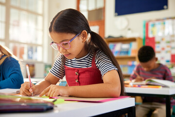 Little multiethnic girl writing on notebook at primary school