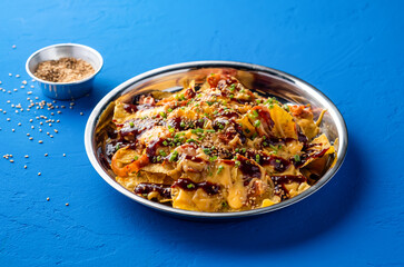 Loaded Fries Nachos with Kimchi, Chicken, Cheese, Sauce, sesame seeds and green onion served in plate isolated on blue background side view of unhealthy fast food